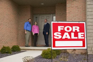Couple and businessman in front of home, For Sale sign in foreground