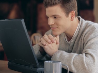 A young man resting head on hands looking at laptop computer