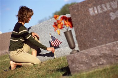 Woman placing flag by cemetery headstone