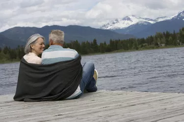 Mature couple sitting on pier wrapped with blanked, mountain range in background