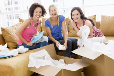 Three girl friends unpacking boxes in new home smiling