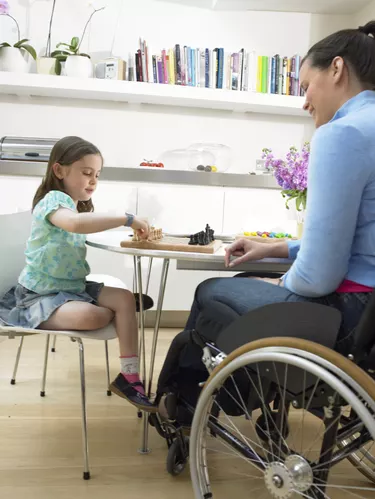 Mother sitting in wheelchair playing chess with daughter (6-8) at table