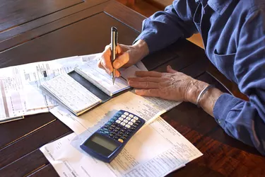 Close-up of a mature woman's hands as she sits at a table writes checks.