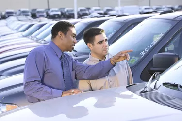 A salesman points out features of a new car to an interested customer