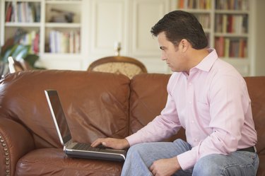 Side profile of a mid adult man sitting on a couch working on a laptop