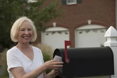 Smiling senior woman putting mail from her mailbox