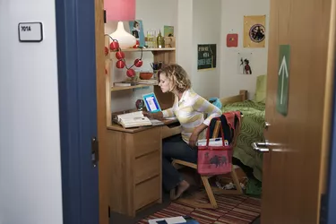 Young woman working at desk in student dorm, view through open door