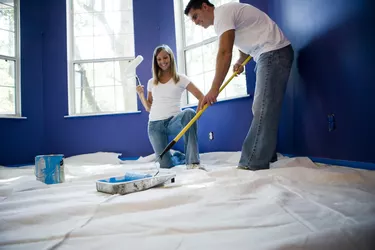 Young woman holding paint roller while young man preparing color