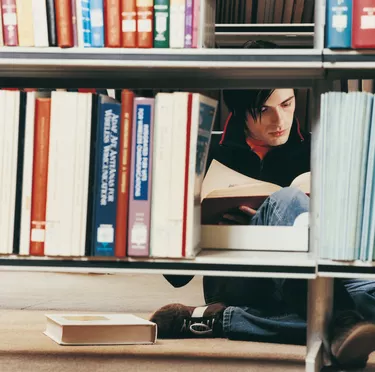 Male University Student Reading in a Library Behind Shelves