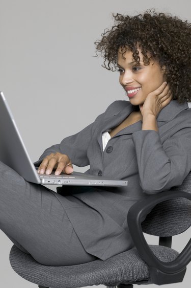 business portrait of a young adult female in a grey suit as she uses her laptop computer