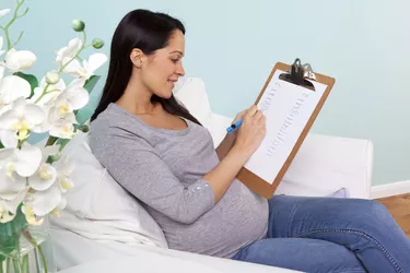 Pregnant woman sitting in a chair writing baby names