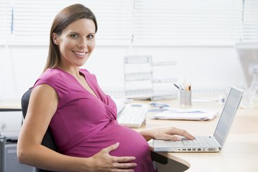 Pregnant woman at work using laptop and smiling