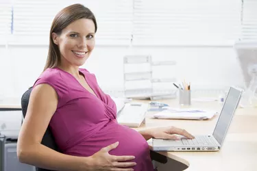 Pregnant woman at work using laptop and smiling