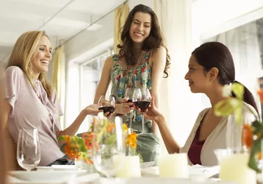 Three women raising glasses of red wine at dinner party, smiling