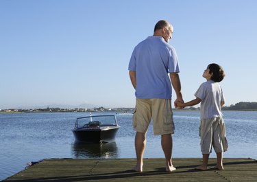 Father and son (6-8) holding hands on jetty, rear view