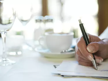 Woman in restaurant holding pen to paper, close-up of hand