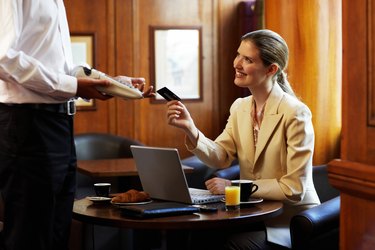 Young businesswoman at cafe table, paying waiter by credit card
