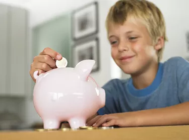 Boy (7-9) putting euro coin into piggy bank, smiling