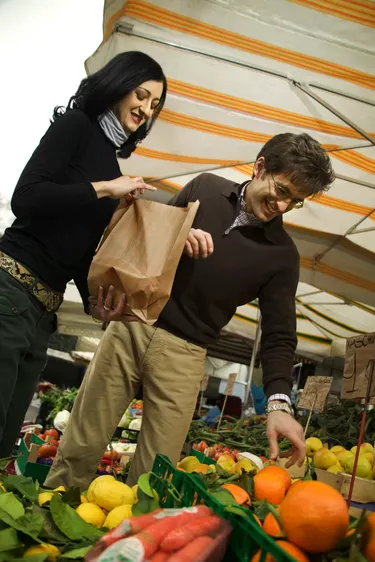 Low angle of a couple adding fruit to a bag while shopping in an outdoor fresh market in Italy.