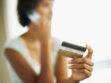 close-up of a young woman talking on a mobile phone while holding a credit card