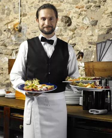 Waiter holding three plates of salad, smiling, portrait