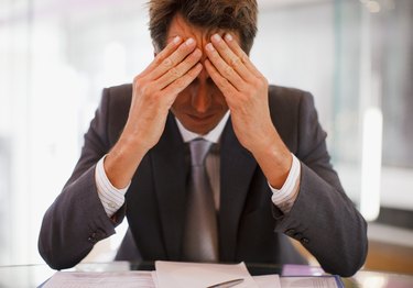 Frustrated businessman sitting at desk with  head in hands