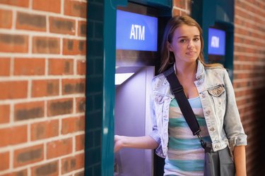 Pretty happy student withdrawing cash smiling at camera