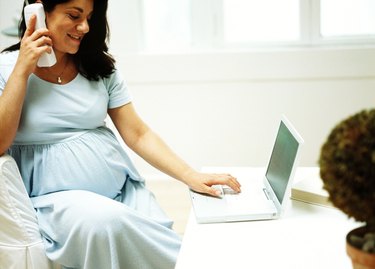view of a pregnant woman talking on the phone and working on a laptop