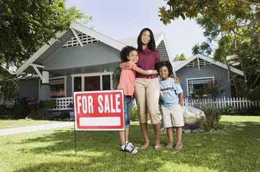 Mother and children with For Sale sign in front of house