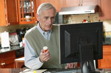 Man using computer at home and holding prescription bottle