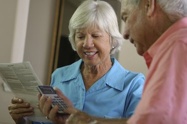 Senior man using a calculator with a senior woman sitting beside him