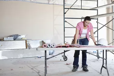 Front view of young female contractor looking at building plans at table