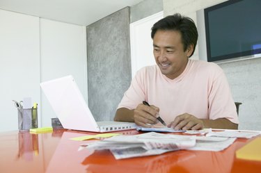 Man Sits at His Desk Working From Home, Using His Laptop