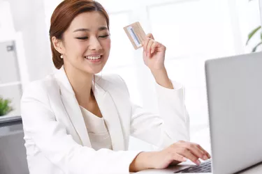 Young business lady holding credit card in front of laptop