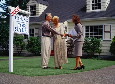 Mature couple and real estate agent standing in front of sold house