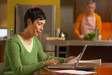 Woman paying bills while man washes lettuce