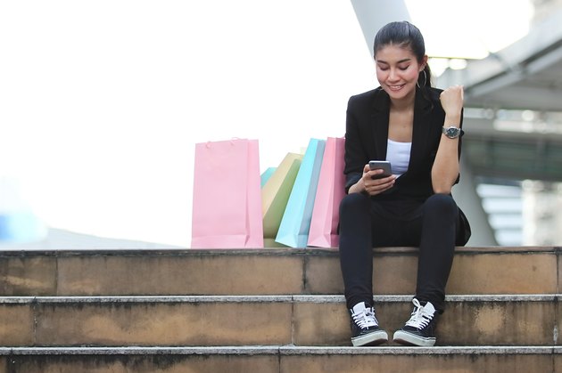 Cheerful young Asian woman looking mobile smart phone at outdoors. Shopping online concept.