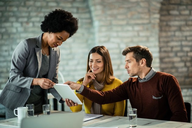 African American financial consultant and couple cooperating while using touchpad on a meeting.