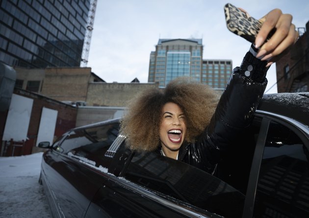 Exuberant young woman taking selfie in limousine window