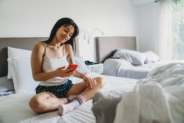 Young adult woman using a smartphone while she's lying on the bed