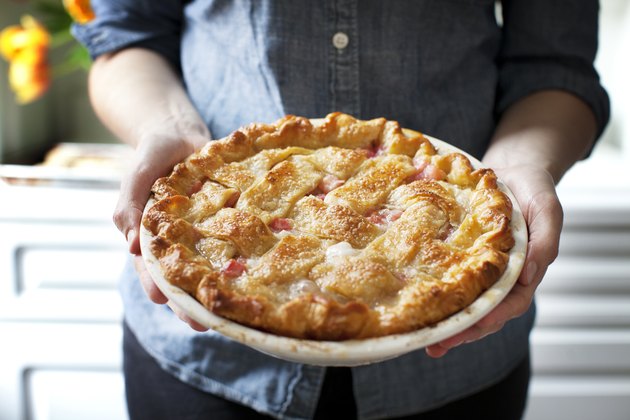 Midsection of woman holding baked rhubarb pie while standing at home