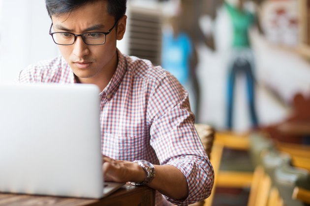 Serious young Asian student using laptop in cafe