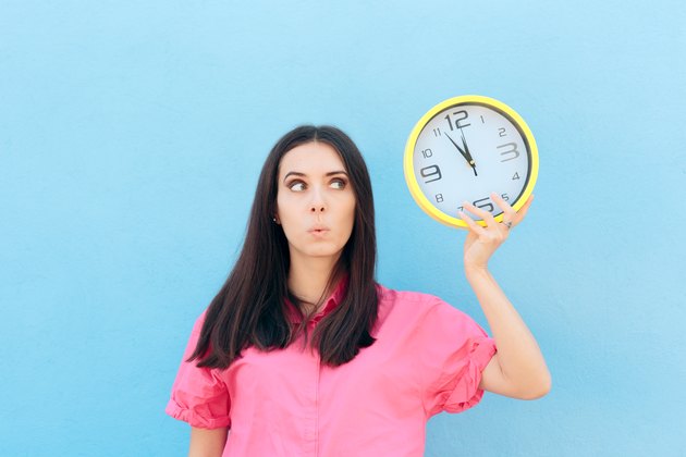 Cheerful Woman Holding a Clock on a Blue Background