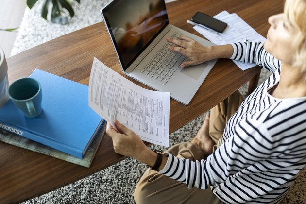 Mature woman with documents using laptop at home