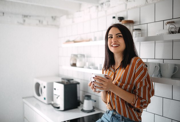 Young woman sitting on kitchen counter and enjoying morning coffee