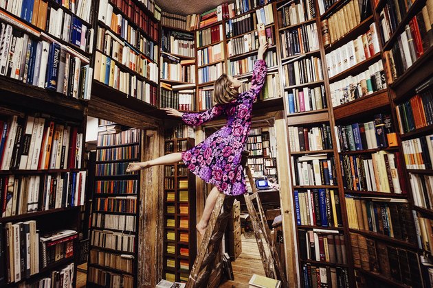 Carefree woman on ladder reaching for book in library