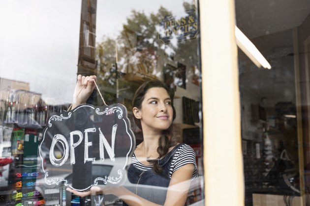 Confident female small business owner hanging Open sign in shop window