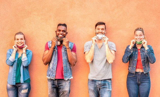 Multiracial millennial friends smiling with face mask after lockdown reopening - Happy guys and girls having fun around old town streets - University students on travel vacation - Warm bright filter
