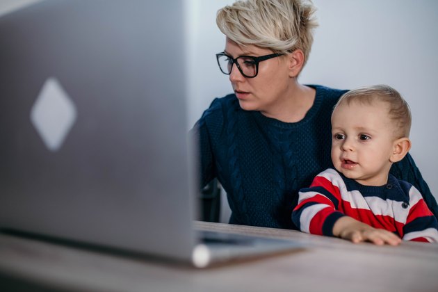 business, motherhood, multi-tasking, family and people concept - happy smiling businesswoman with baby and laptop computer working at office