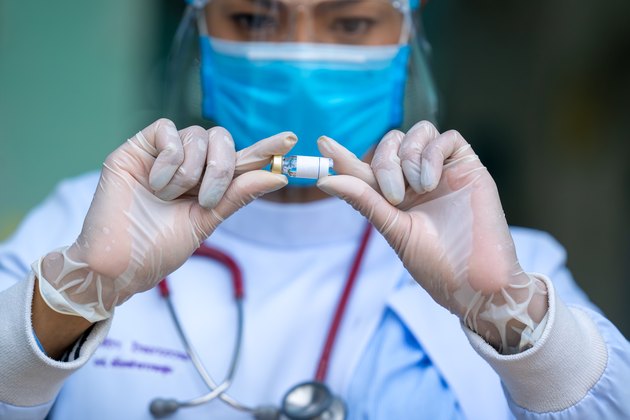 Female doctor wearing protective mask to Protect Against Covid-19 looking medicine vial vaccine bottle on hand holding.